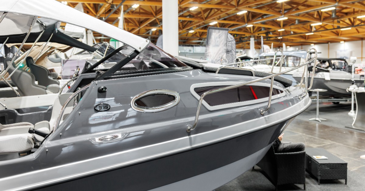 Gray luxury motorboat with chrome railings and a white canopy displayed among other boats inside a large showroom.